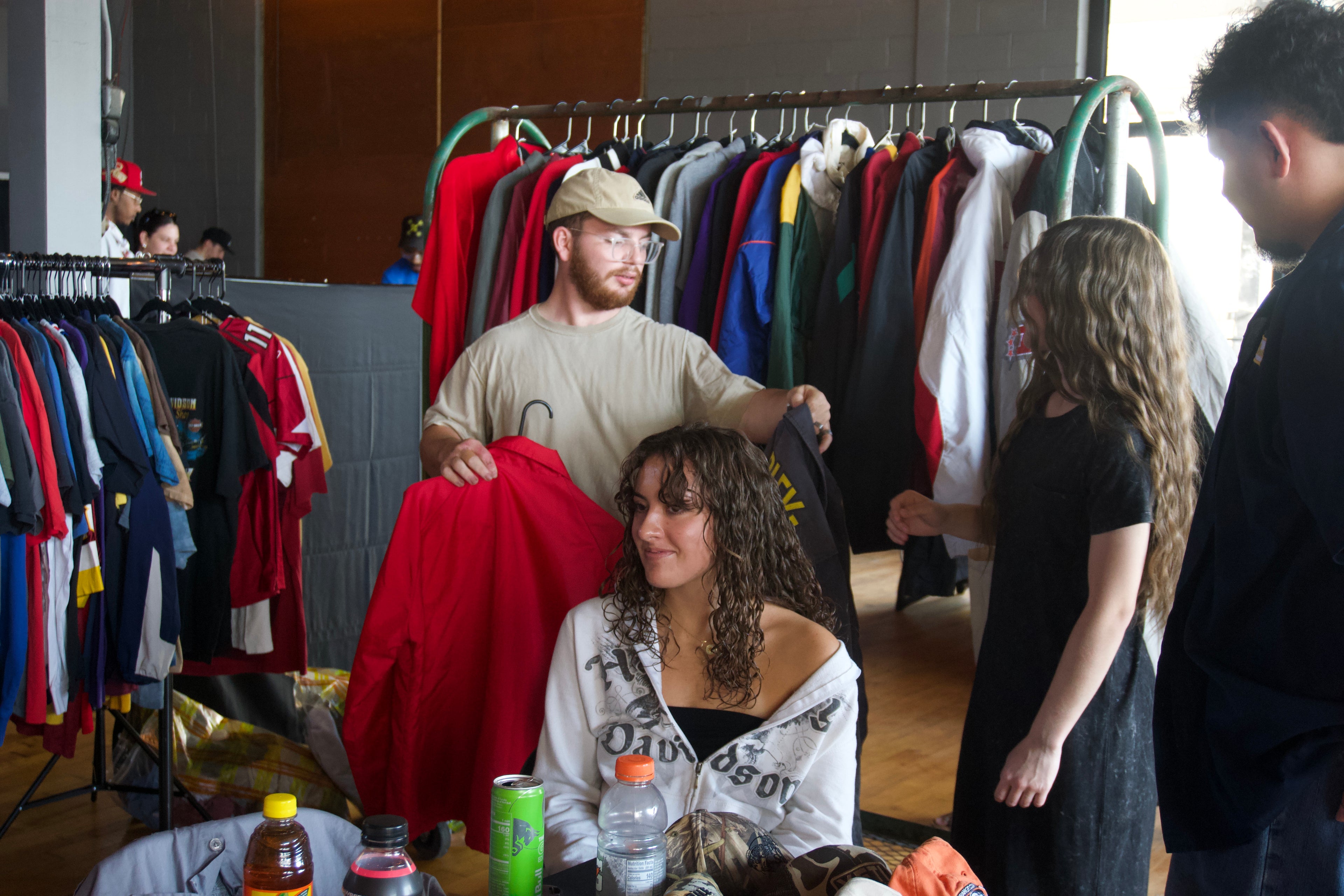 People shopping in a clothing store with racks of clothes and a man holding a red jacket.